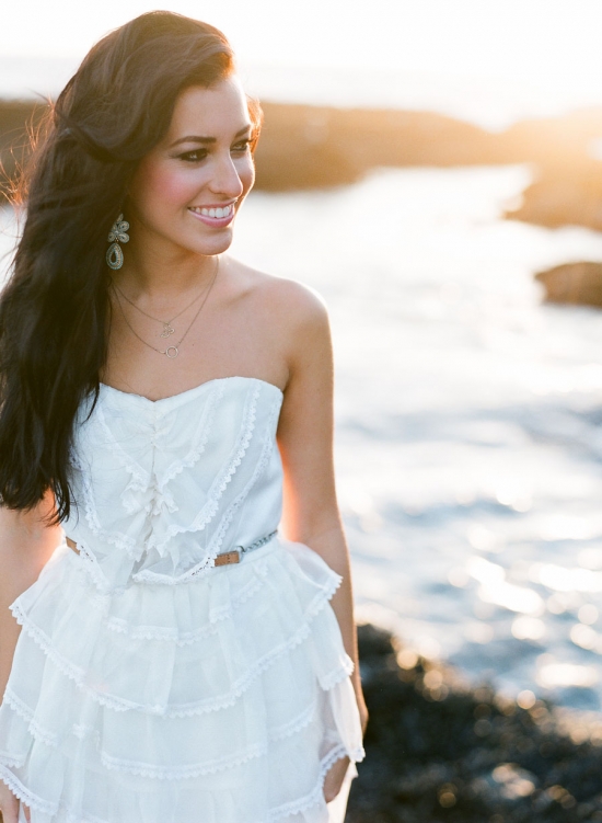 Woman in white dress smiles by the ocean at sunset