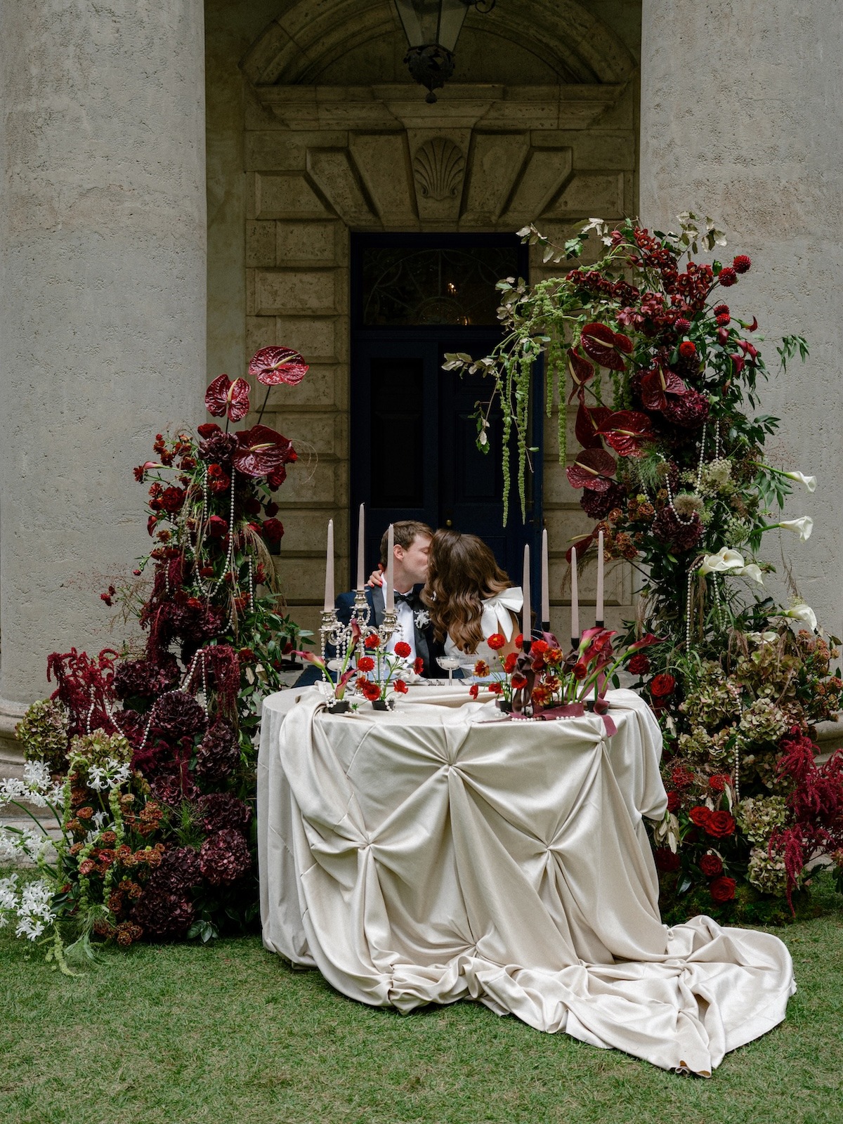 couple kissing at sweetheart table with deep red flowers